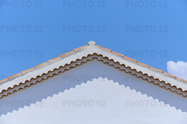 Top of a white painted house with a red tiled roof against a clear blue sky, summer,