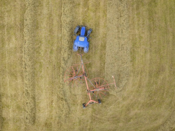 An aerial view shows a tractor with a hay tedder ploughing patterns into a hay field, Dachtel.