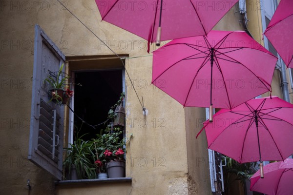 In the perfume town of Grasse, red umbrellas hang between the houses, on the left a window with