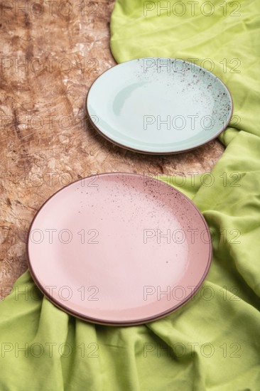 Two empty blue and pink plates on brown concrete background and green textile. Side view, close up