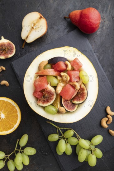 Vegetarian fruit salad of watermelon, grapes, figs, pear, orange, cashew on slate board on a black