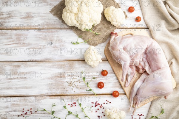 Whole raw rabbit with cauliflower, tomatoes and spices on a white wooden background and linen