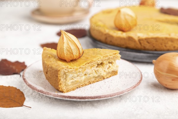 Autumn onion pie decorated with leaves and cup of coffee on gray concrete background. Side view,