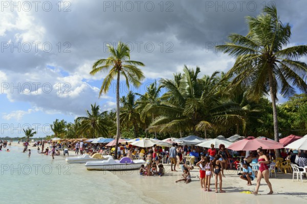 Beachgoers relax under colourful umbrellas next to the calm sea, Boca Chica, Santo Domingo
