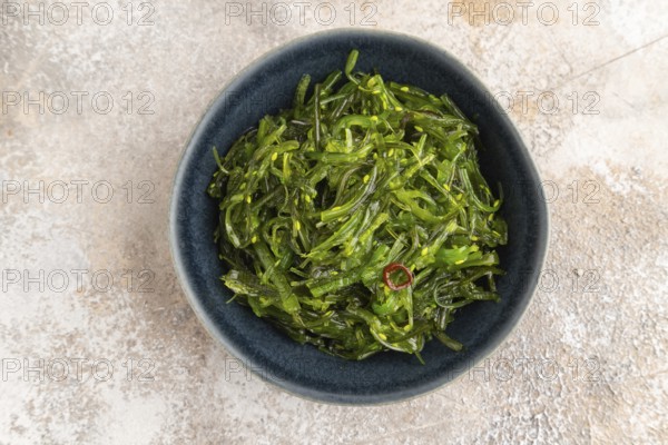 Chuka seaweed salad in blue ceramic bowl on brown concrete background. Top view, flat lay