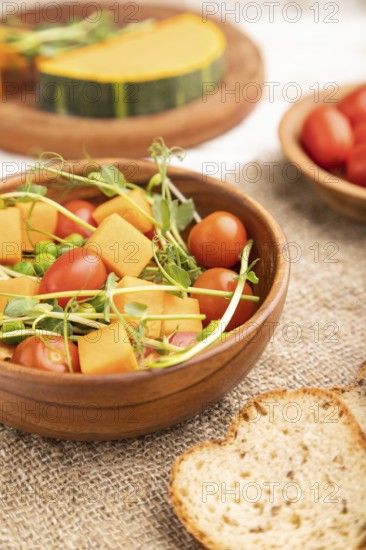 Vegetarian vegetable salad of tomatoes, pumpkin, microgreen pea sprouts on white wooden background
