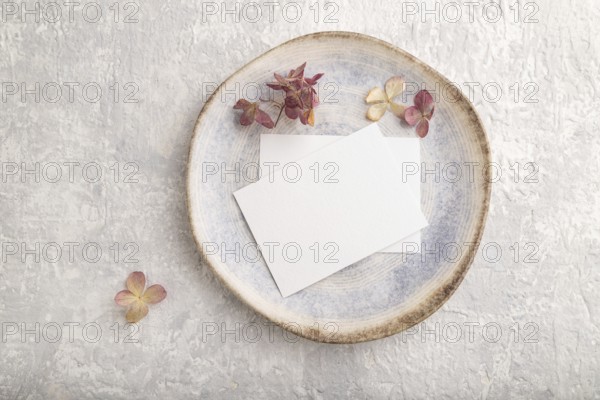White paper invitation card, mockup with dried hydrangea flowers on ceramic plate and gray concrete