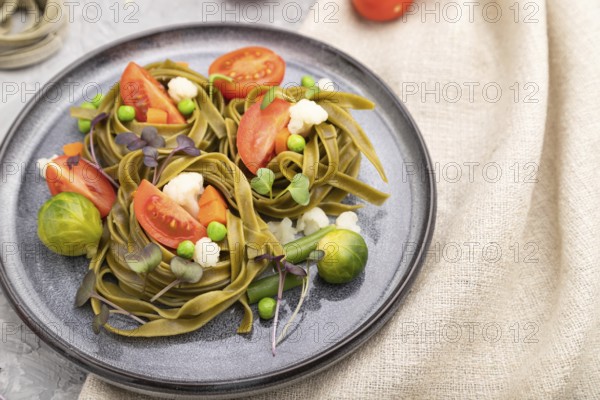 Tagliatelle green spinach pasta with tomato, pea and microgreen sprouts on a gray concrete