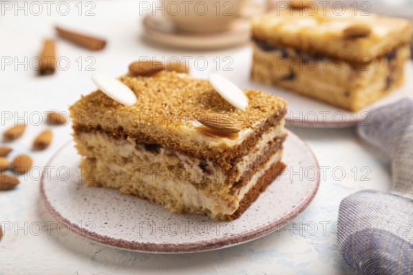 Honey cake with milk cream, caramel, almonds and a cup of coffee on a white concrete background and