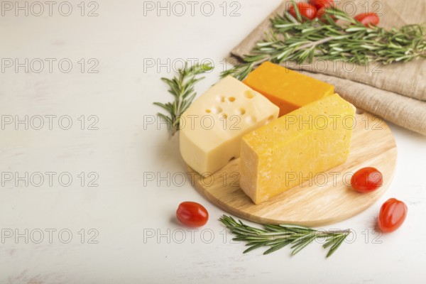 Various types of cheese with rosemary and tomatoes on wooden board on a white wooden background and