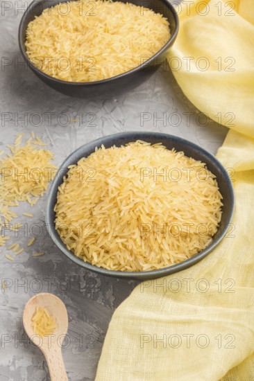 Blue ceramic bowl with raw golden rice and wooden spoon on a gray concrete background and yellow