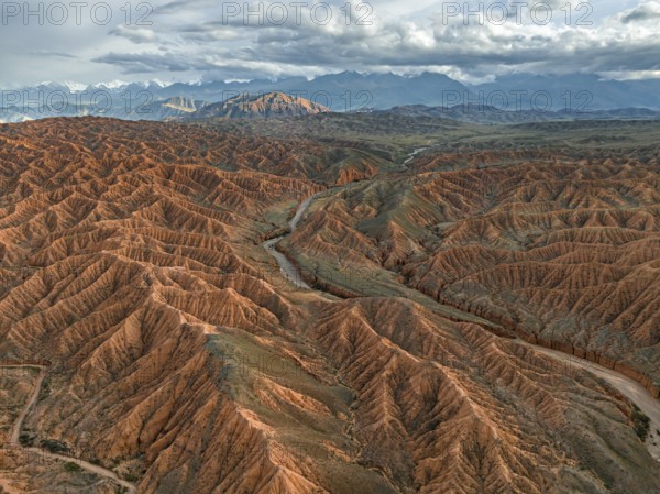 River bed runs through a landscape of eroded hills, badlands at sunset, mountain peaks of the Tian