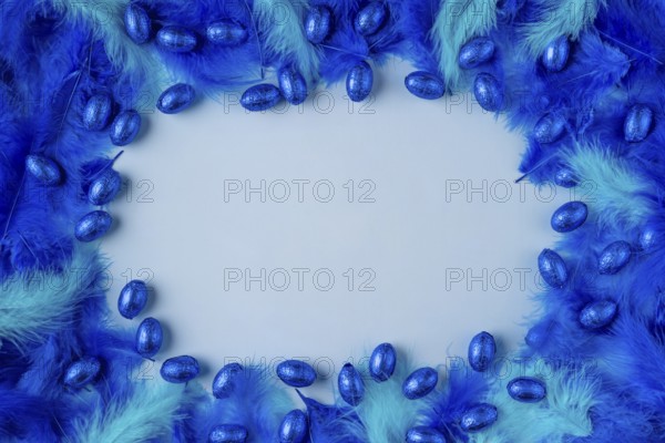 Frame made of blue and turquoise feathers with blue chocolate eggs on a light blue background