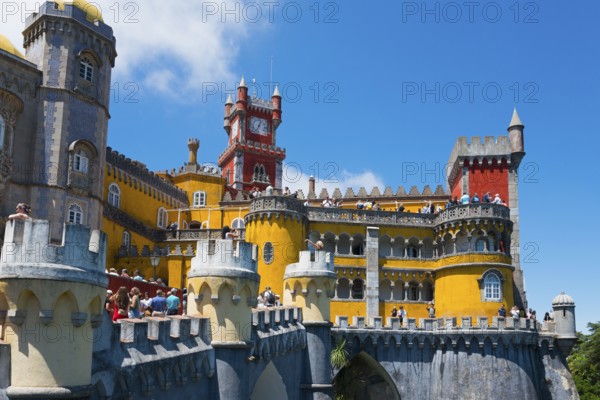Colourful castle with yellow, red and grey towers, blue sky and visitors, Palácio Nacional da Pena,