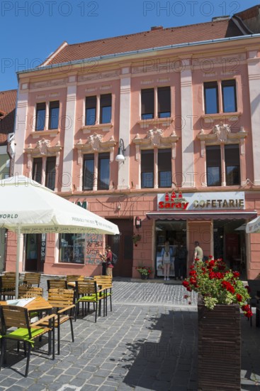 Street view of a pink façade with elaborate stucco details and a café in the foreground, town house