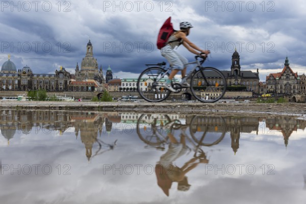The Dresden silhouette with a cyclist and dark clouds behind the Church of Our Lady is reflected in