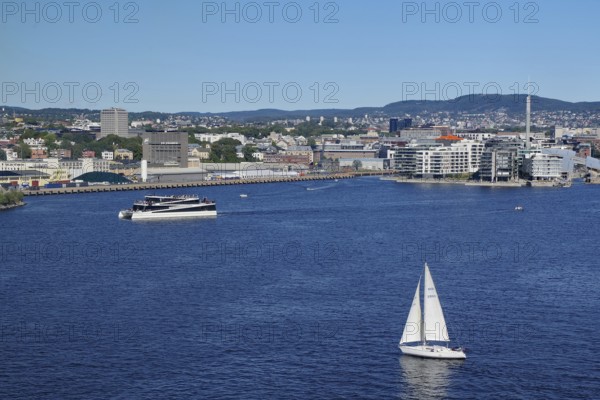 Urban coastal view with a sailing boat, modern harbour and surrounding buildings, electric ferry,