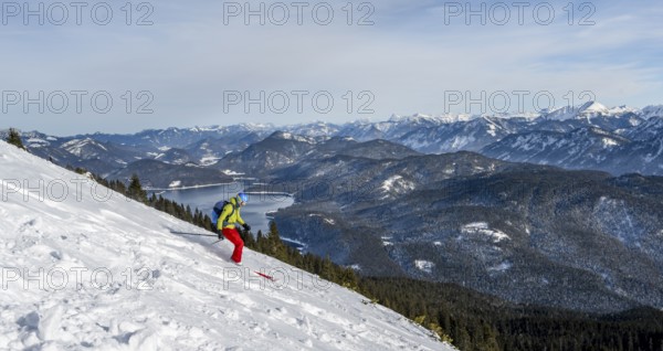 Skiers skiing down the Simetsberg, view of Walchensee and mountain panorama, Estergebirge, Bavarian