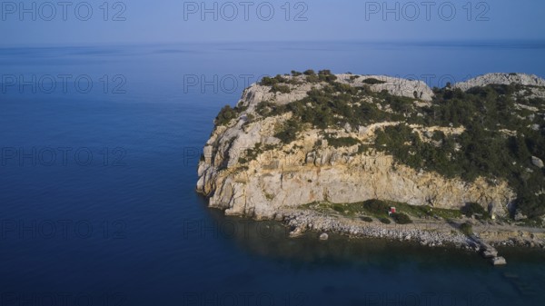 A drone shot shows a remote coastal strip with steep cliffs at the edge of the clear blue sea,