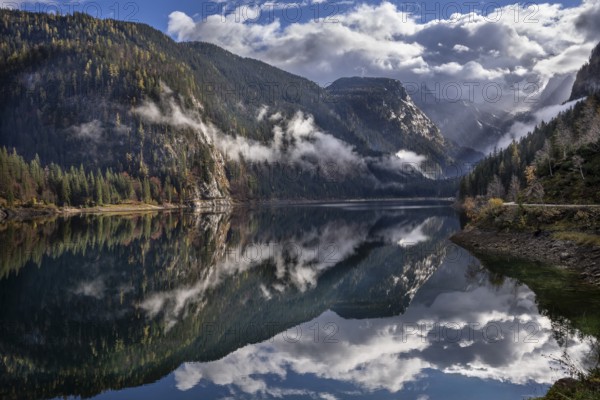 The Vordere Gosausee in autumn. In the background, the Dachstein mountain range in clouds. Partly