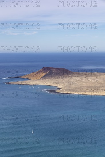 Island La Graciosa with volcanic cone and sailing boats in front of the coast and clear sky in the