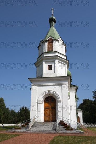 Detailed view of a white church with a green tower, surrounded by landscaped paths under a blue