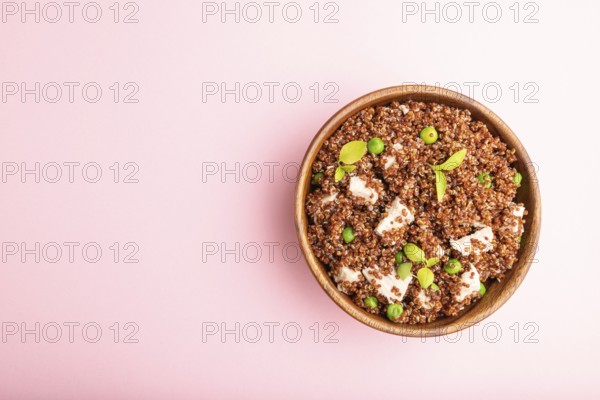 Quinoa porridge with green pea and chicken in wooden bowl on a pastel pink background. Top view,
