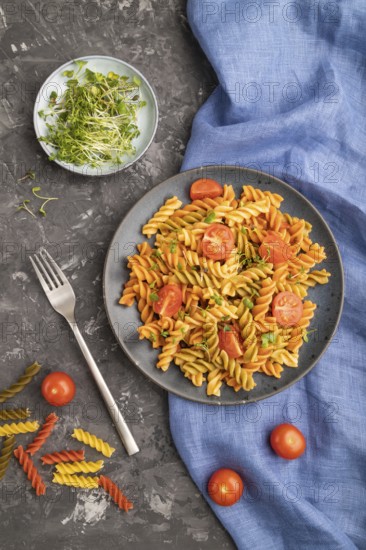 Tortiglioni semolina pasta with tomato and microgreen sprouts on a black concrete background and