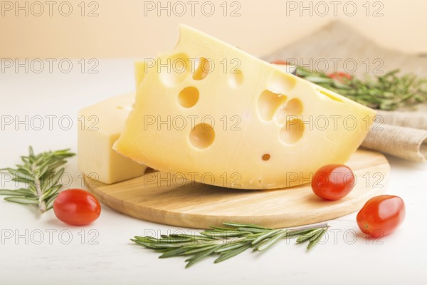 Various types of cheese with rosemary and tomatoes on wooden board on a white wooden background and