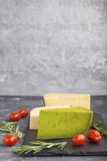 Green basil cheese and various types of cheese with rosemary and tomatoes on black slate board on a