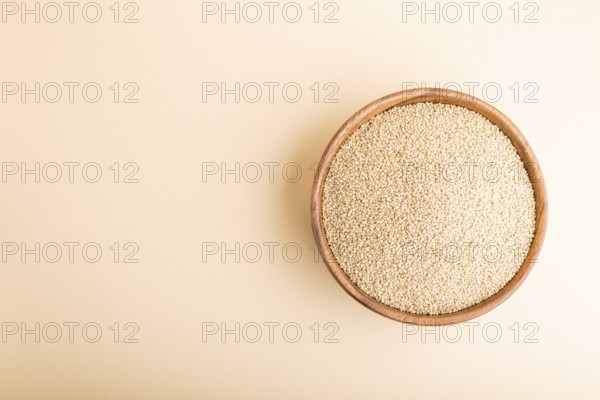 Wooden bowl with raw white quinoa seeds on a pastel orange background. Top view, flat lay, copy