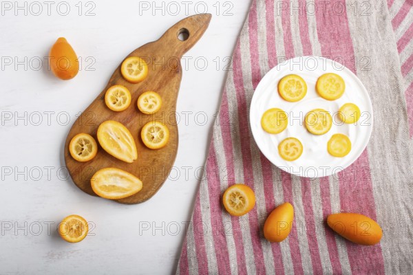 Greek yogurt with kumquat pieces in a white plate on a white wooden background, copy space