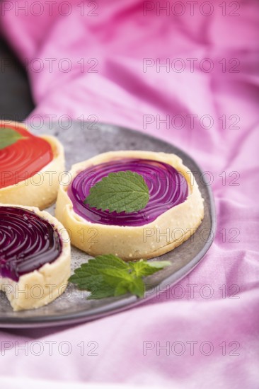 Sweet tartlets with jelly and milk cream with cup of coffee on a black concrete background and pink