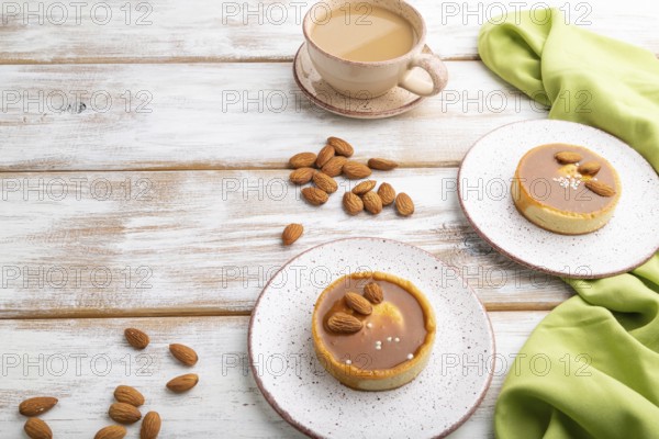 Sweet tartlets with almonds and caramel cream with cup of coffee on a white wooden background and