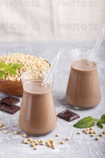 Organic non dairy soy chocolate milk in glass and wooden plate with soybeans on a gray concrete