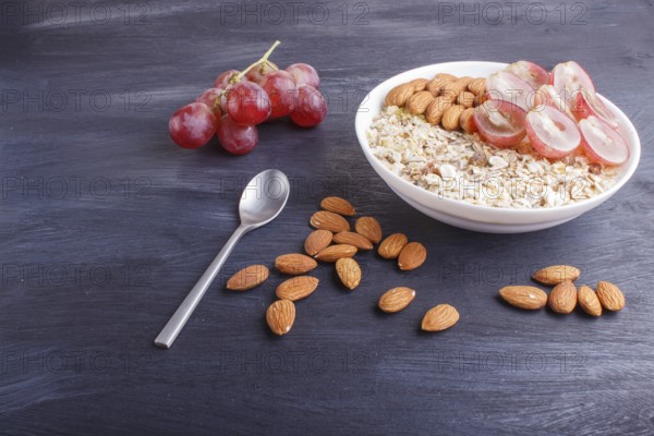 A plate with muesli, almonds, pink grapes on a black wooden background. close up. copy space