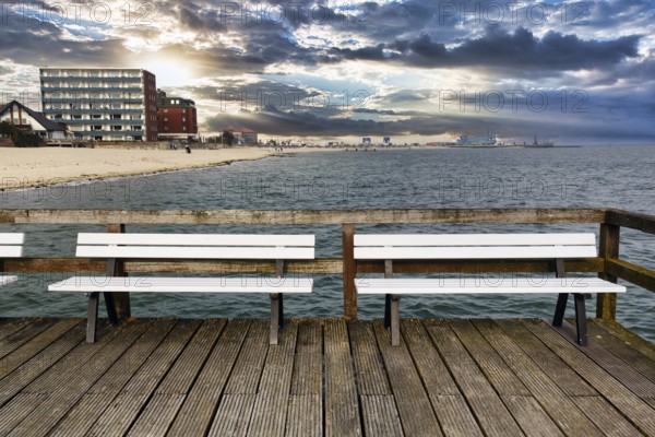 Empty benches on the pier with a view of the beach, houses and ferry port, autumn weather, Wyk auf