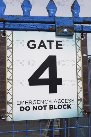 Close-up of posted emergency access gate 4 Do Not Block notice sign on blue painted steel and wire