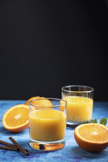 Glass of orange juice on a black and blue background. Hard light, contrast. Side view, copy space