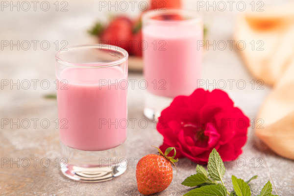 Sweet strawberry liqueur in glass on a gray concrete background and orange textile. side view,