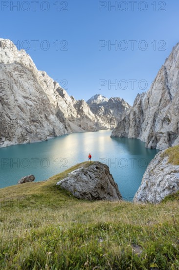 Young man at the turquoise mountain lake Kol Suu with rocky steep mountains, Kol Suu Lake, Sary
