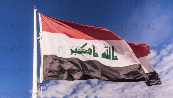 The flag of Iraq flutters in the wind, isolated against a blue sky