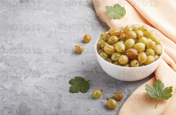 Fresh green gooseberry in white bowl with orange textile on gray concrete background. side view,