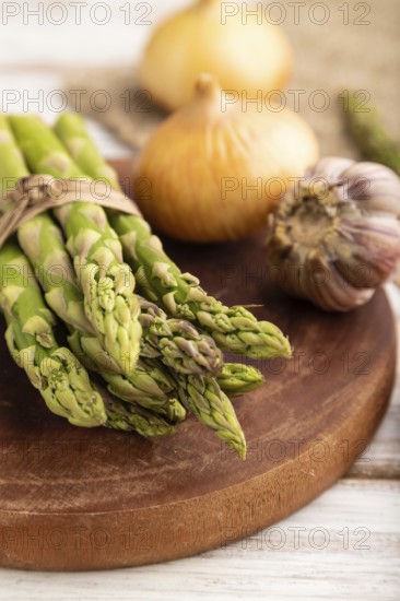 Bunch of fresh green asparagus, garlic, onion on white wooden background. Side view, selective