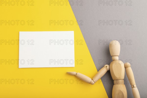 Wooden mannequin holding white blank poster on gray and yellow pastel background. copy space,