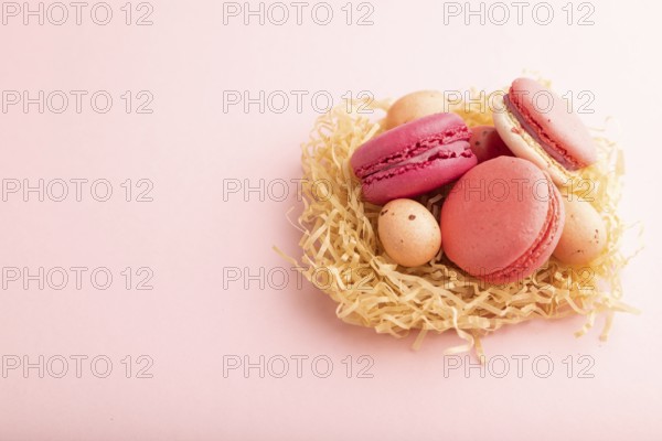 Purple and pink macaroons and chocolate eggs in decorative paper nest on pink pastel background.
