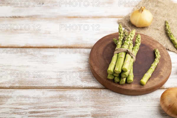 Bunch of fresh green asparagus, garlic, onion on white wooden background. Side view, copy space.