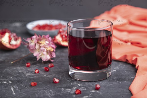 Glass of pomegranate juice on a black concrete background with red textile. Side view, close up,