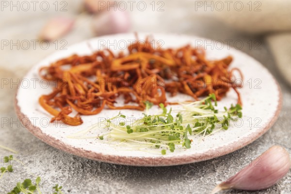 Fried Cordyceps militaris mushrooms on brown concrete background with microgreen, herbs and spices.