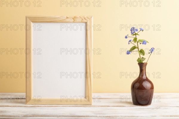 Wooden frame with blue forget-me-not flowers in ceramic vase on orange pastel background. side